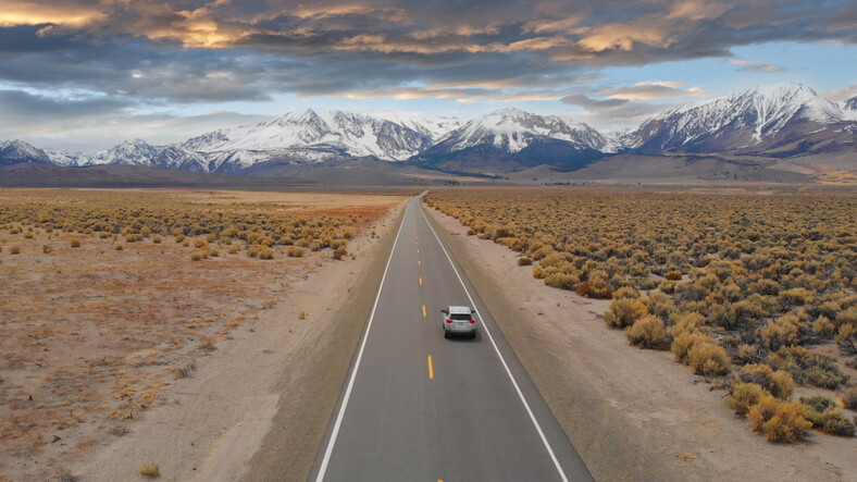 Aerial of open road with car and snowy mountains Aerial of open road with car and snowy mountains