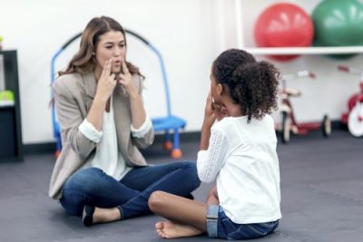 SLP therapist and child patient touching sides of mouths SLP therapist and child patient touching sides of mouths