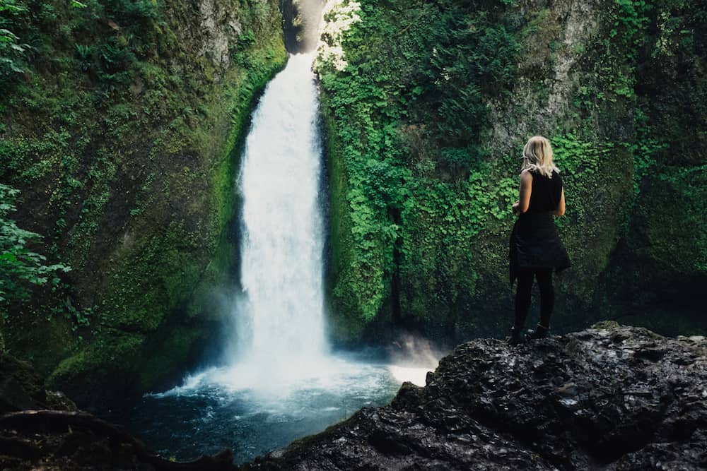 woman standing in front of waterfall woman standing in front of waterfall