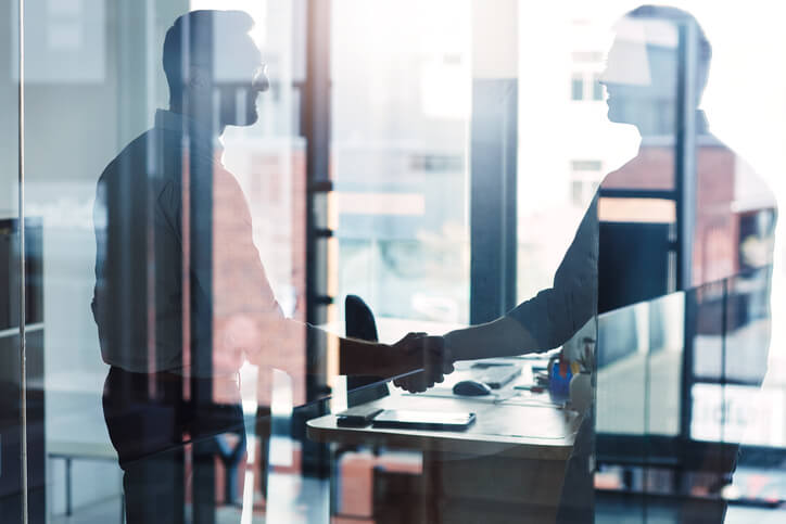 Two men shaking hands in glass office Two men shaking hands in glass office