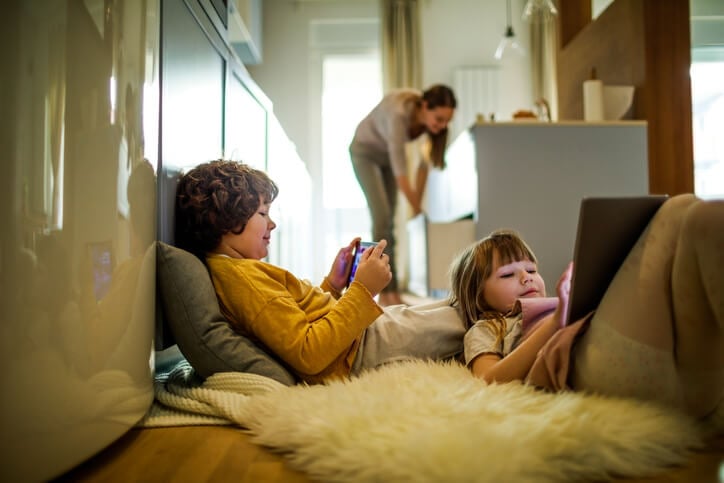 two kids playing on tablets while mom works in kitchen two kids playing on tablets while mom works in kitchen