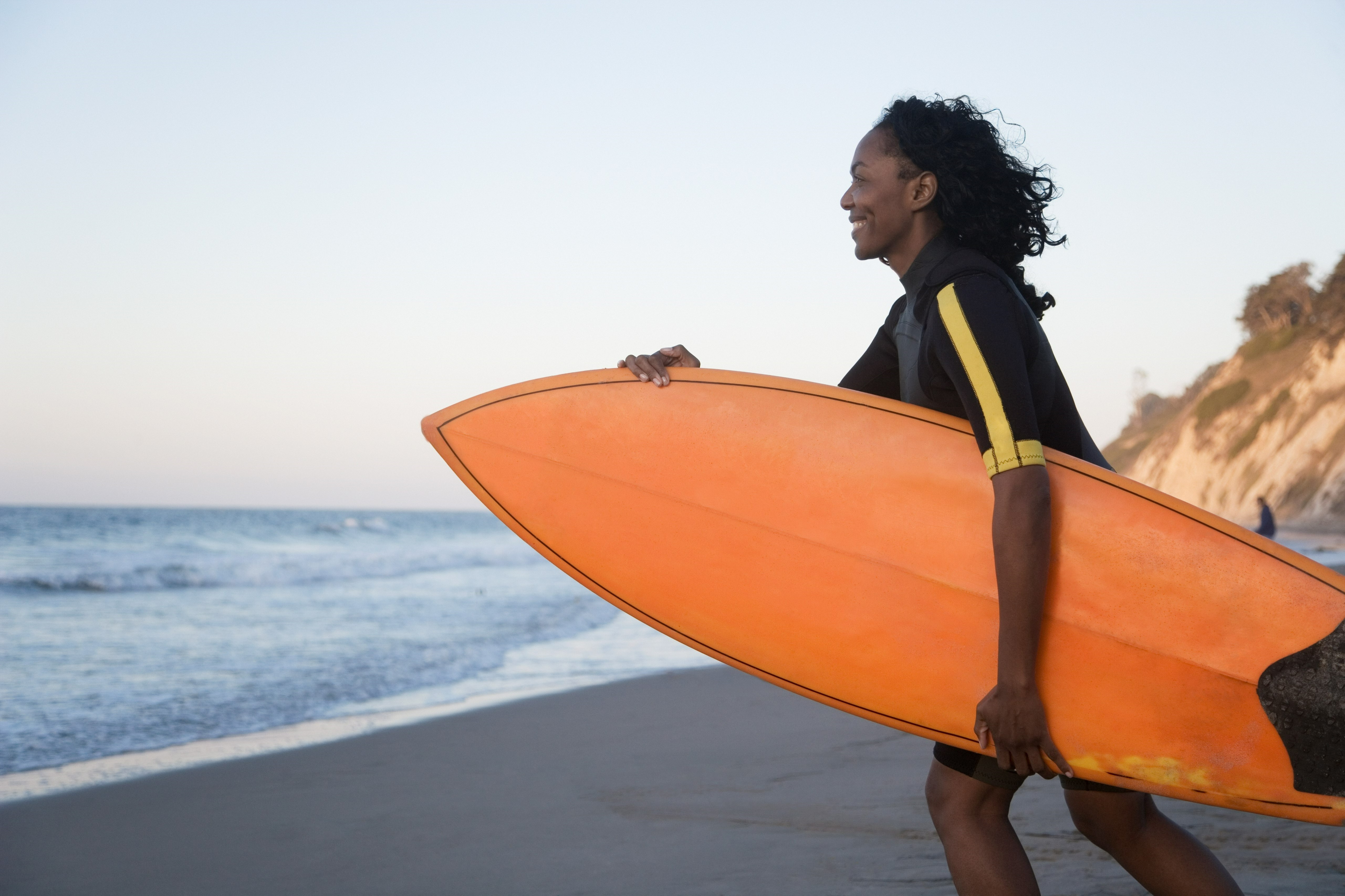 woman smiles as she heads into the ocean with her orange surf board