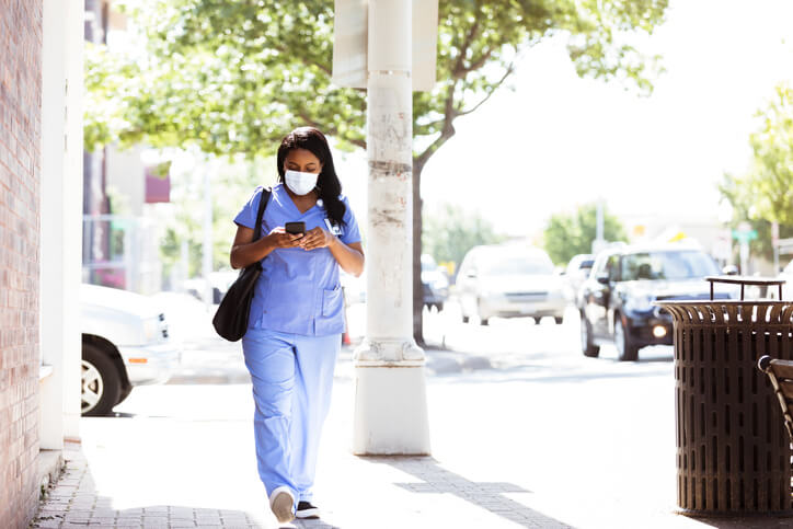 Woman in scrubs and mask walking while looking at phone Woman in scrubs and mask walking while looking at phone