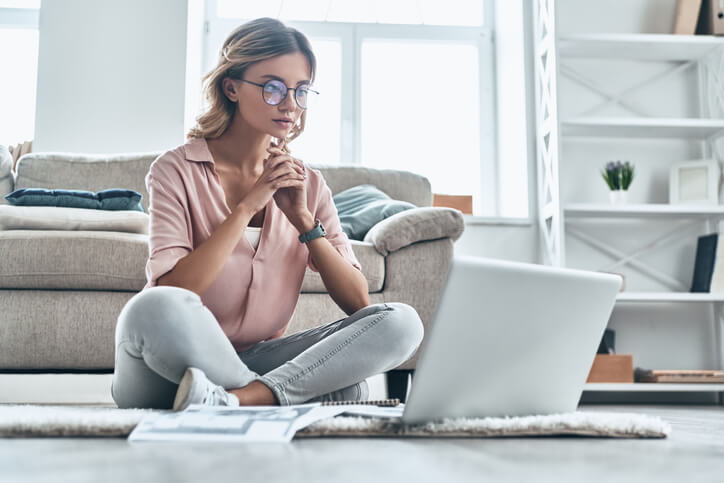 Woman on floor looking at laptop in thoughtful consideration Woman on floor looking at laptop in thoughtful consideration