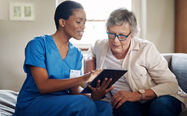 Home health provider discussing something with older woman looking at tablet Home health provider discussing something with older woman looking at tablet