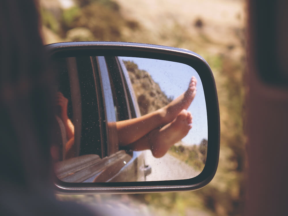 Bare feet relaxing out car window seen in side mirror Bare feet relaxing out car window seen in side mirror