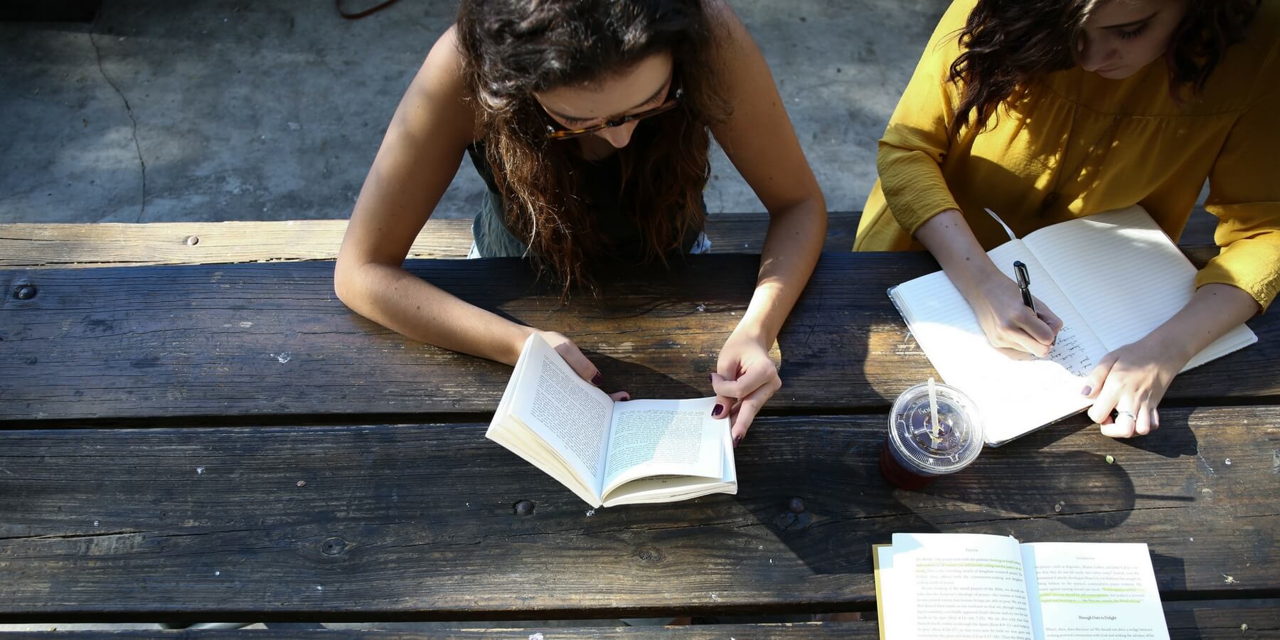 Two young women at table: one reading and one writing Two young women at table: one reading and one writing
