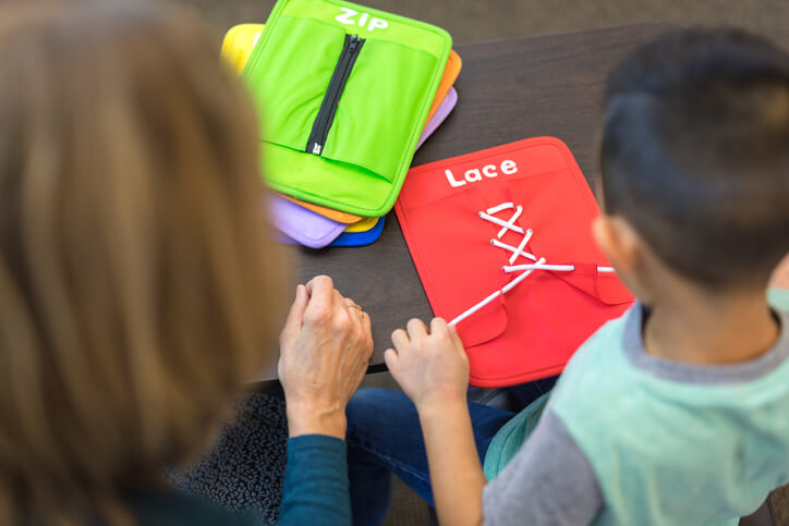 Occupational therapist working with boy on lacing tool Occupational therapist working with boy on lacing tool