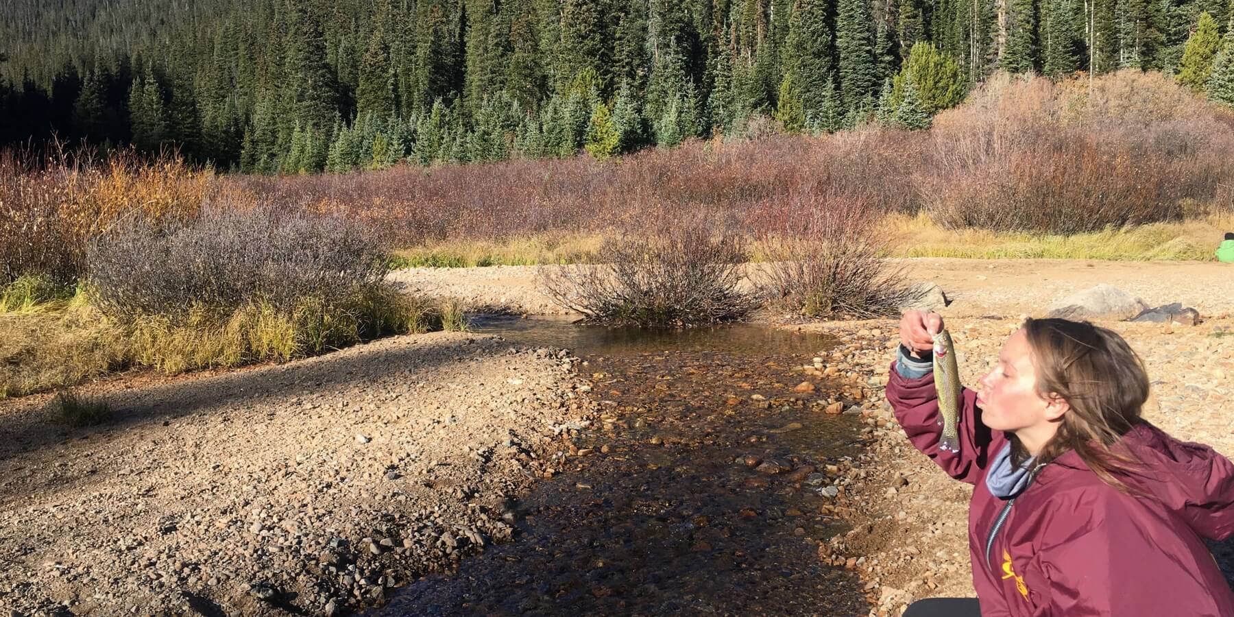 Woman next to rocky stream bed about to kiss a fish Woman next to rocky stream bed about to kiss a fish