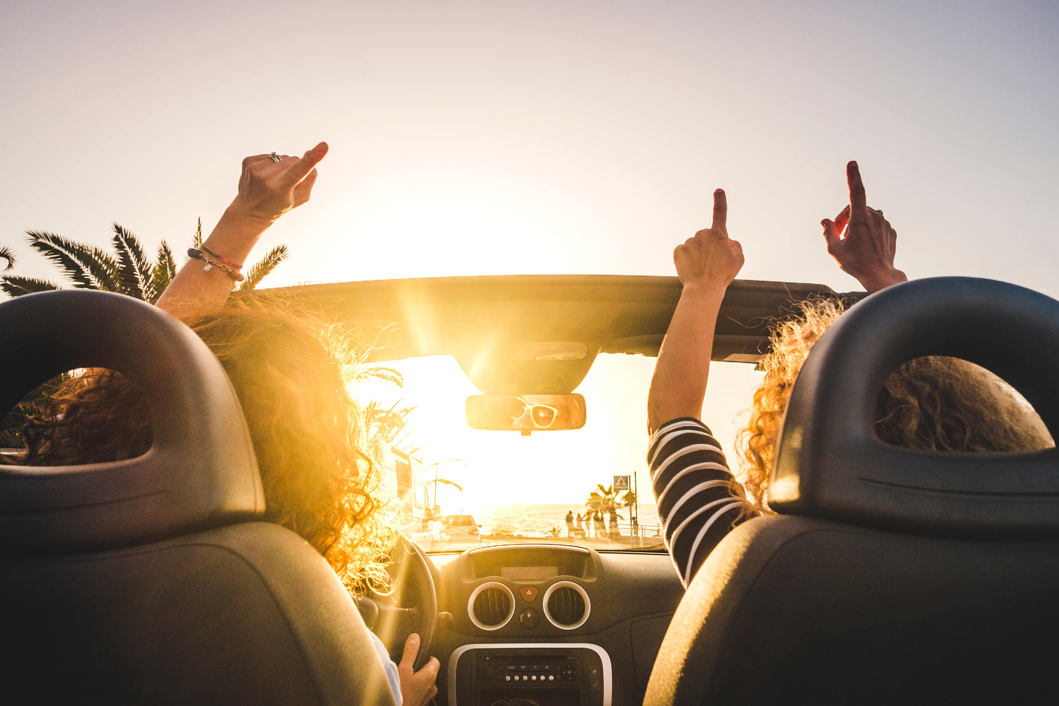 Two friends with arms raised in convertible Two friends with arms raised in convertible