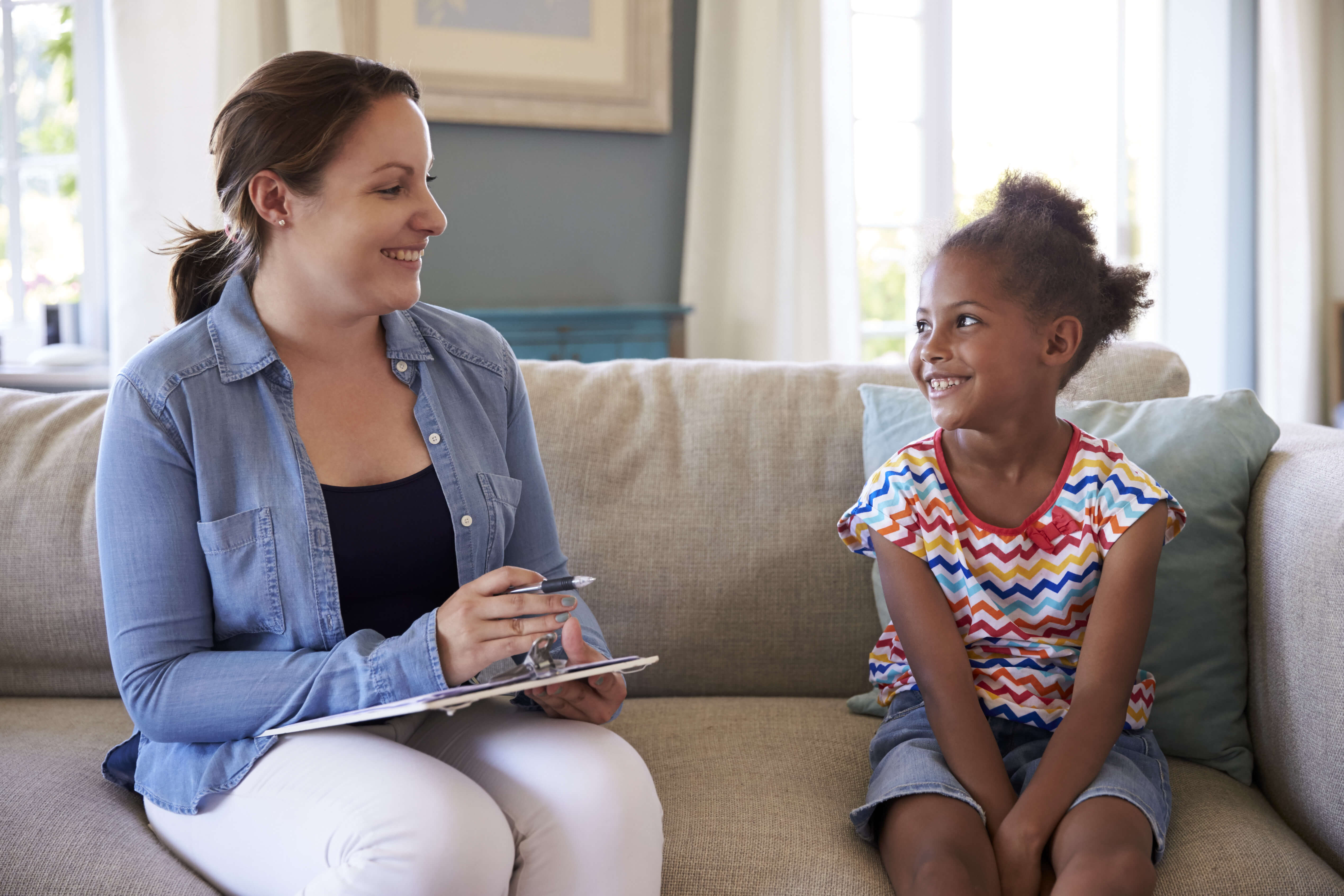 Woman with clipboard talking to child on couch Woman with clipboard talking to child on couch