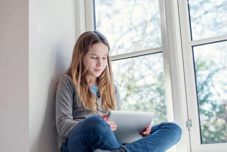 Child sitting in windowsill looking at tablet Child sitting in windowsill looking at tablet