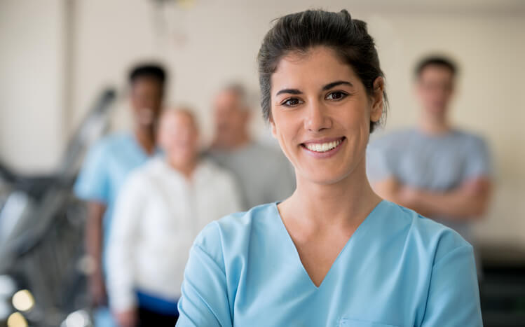Smiling woman in scrubs with diverse blurred group of patients behind Smiling woman in scrubs with diverse blurred group of patients behind