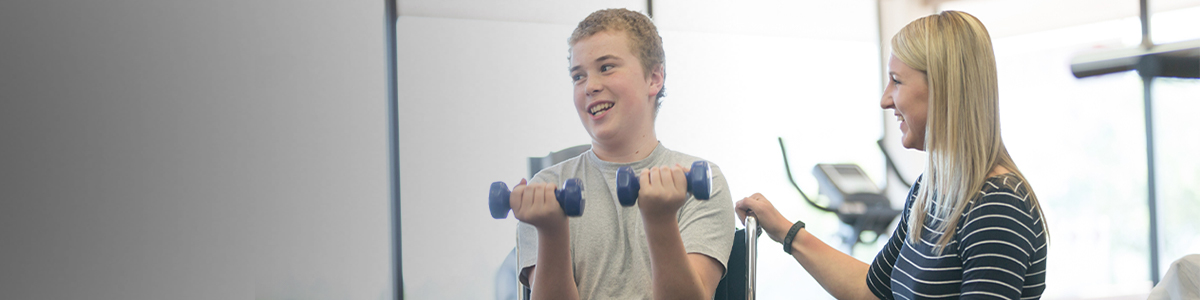 Clinician working with teenager in wheelchair lifting weights