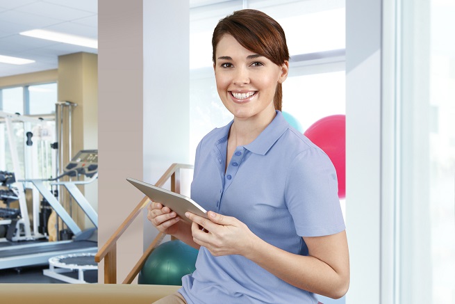 female physical therapist in gym holding ipad and smiling female physical therapist in gym holding ipad and smiling